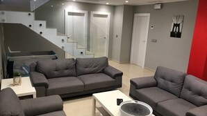 A modern living room with grey sofas, a white coffee table, and a staircase with glass railings.