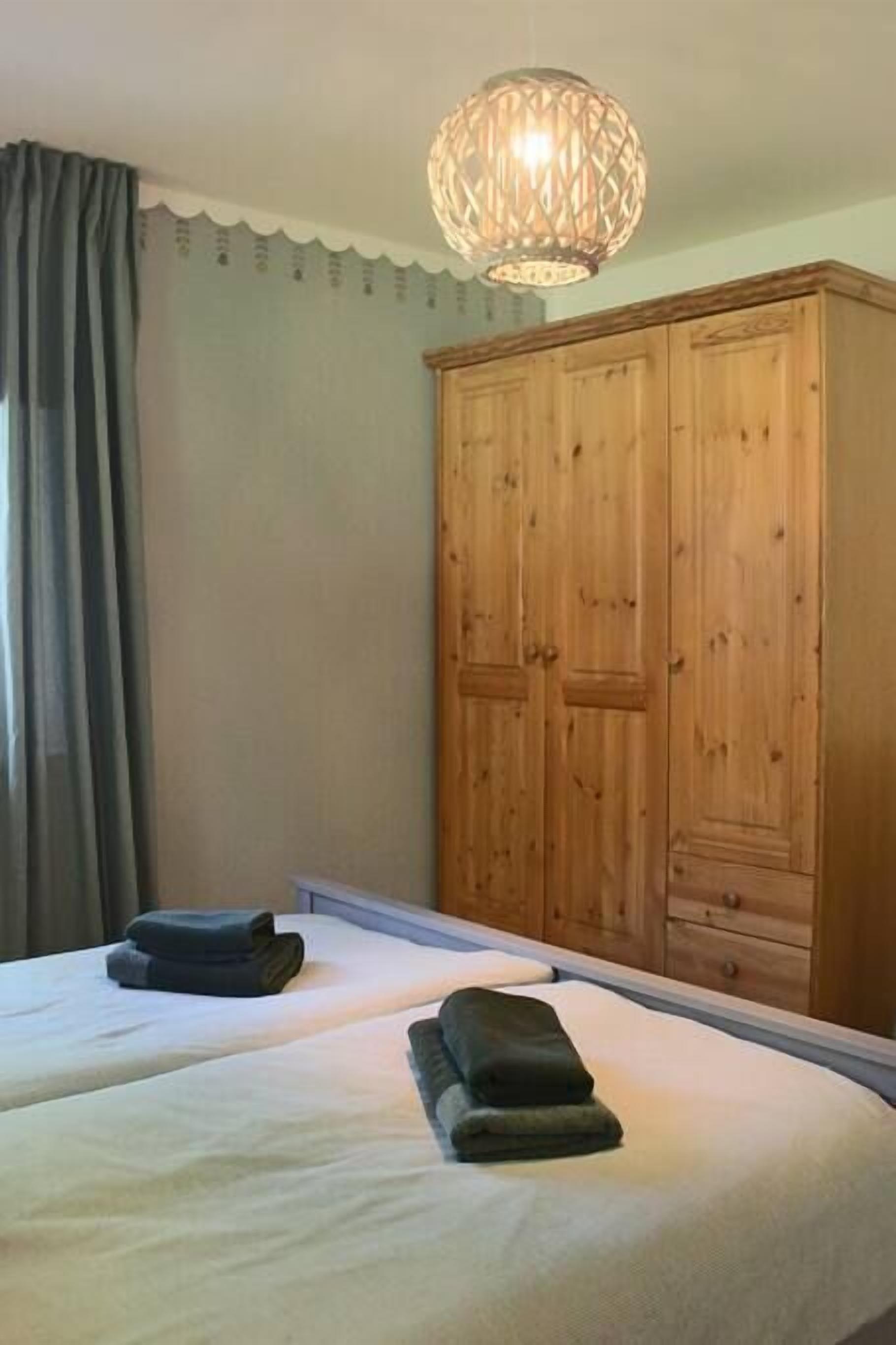 A bedroom with two beds, a wooden wardrobe, and a decorative hanging light fixture.