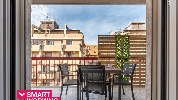 A balcony with a table and chairs, a view of buildings, and a wooden fence. - Appartamento Libertà con terrazza by Wonderful Italy (Palermo)