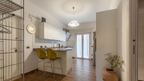 A modern kitchen with wooden flooring, a central island with bar stools, a hanging light fixture, and a large window with curtains. - Appartamento Libertà con terrazza by Wonderful Italy (Palermo)