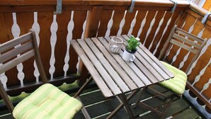 Ein Holztisch mit zwei Stühlen, jeder mit einem Streifenpolster. Auf dem Tisch stehen ein kleiner Topfpflanze und ein Glasbehälter.
