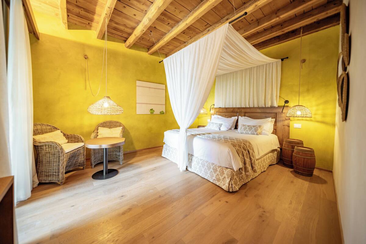 A bedroom with a canopy bed, wicker chairs, a small table, and wooden barrels.