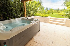 A hot tub in a covered outdoor area with a view of a garden and a grassy field.