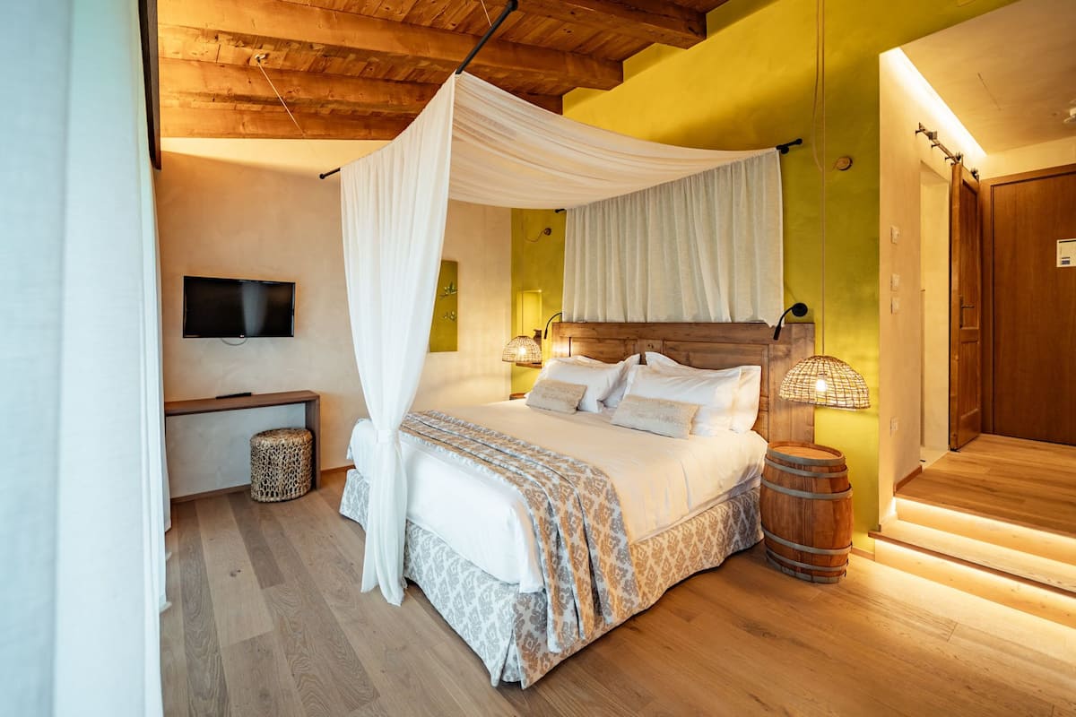 A bedroom with a canopy bed, a television on the wall, a bedside lamp, and a wooden barrel.