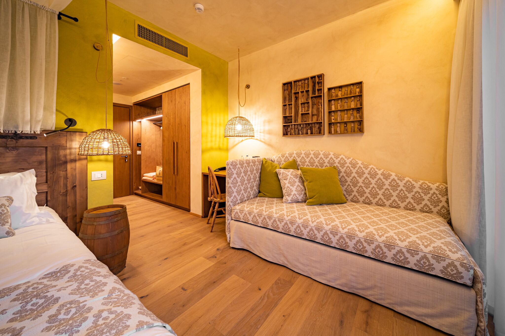 A cozy room with a patterned sofa, a wooden wardrobe, a small table, and a lamp.