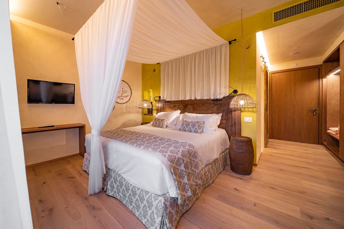 A bedroom with a canopy bed, bedside lamps, a flat-screen TV, and a wooden wardrobe.