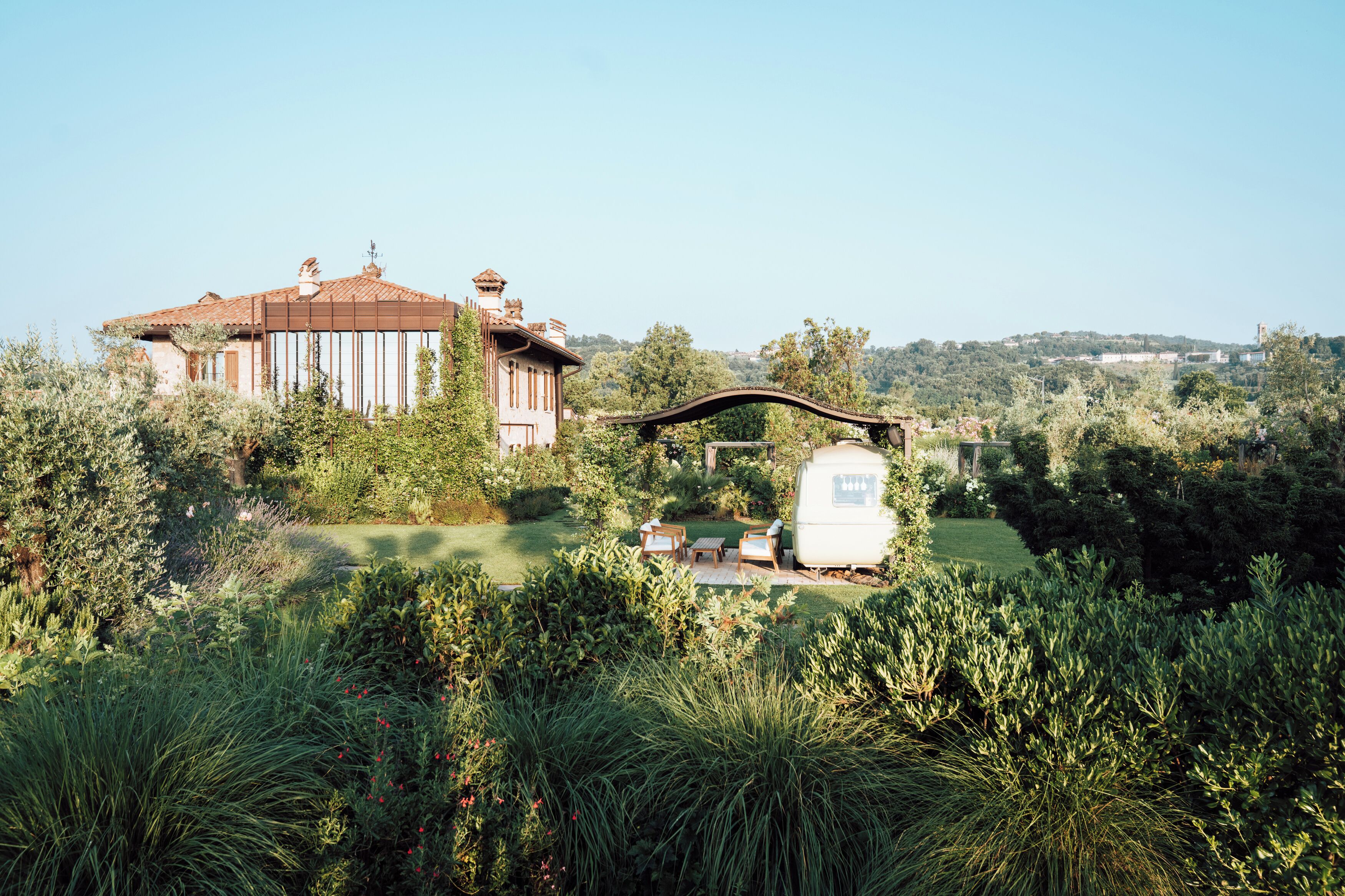 A large house with a garden, a white RV, and a bridge.