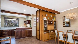 A kitchen with wooden cabinets, a dining area with a table and chairs, and a large window. - Ocean Close - Spacious  Beach House (Guilderton)