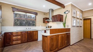 A kitchen with wooden cabinets, a built-in stove, and a window overlooking a garden. - Ocean Close - Spacious  Beach House (Guilderton)