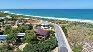 An aerial view of a coastal area with a road curving around a cluster of buildings, some with solar panels, near a beach. - Ocean Close - Spacious  Beach House (Guilderton)