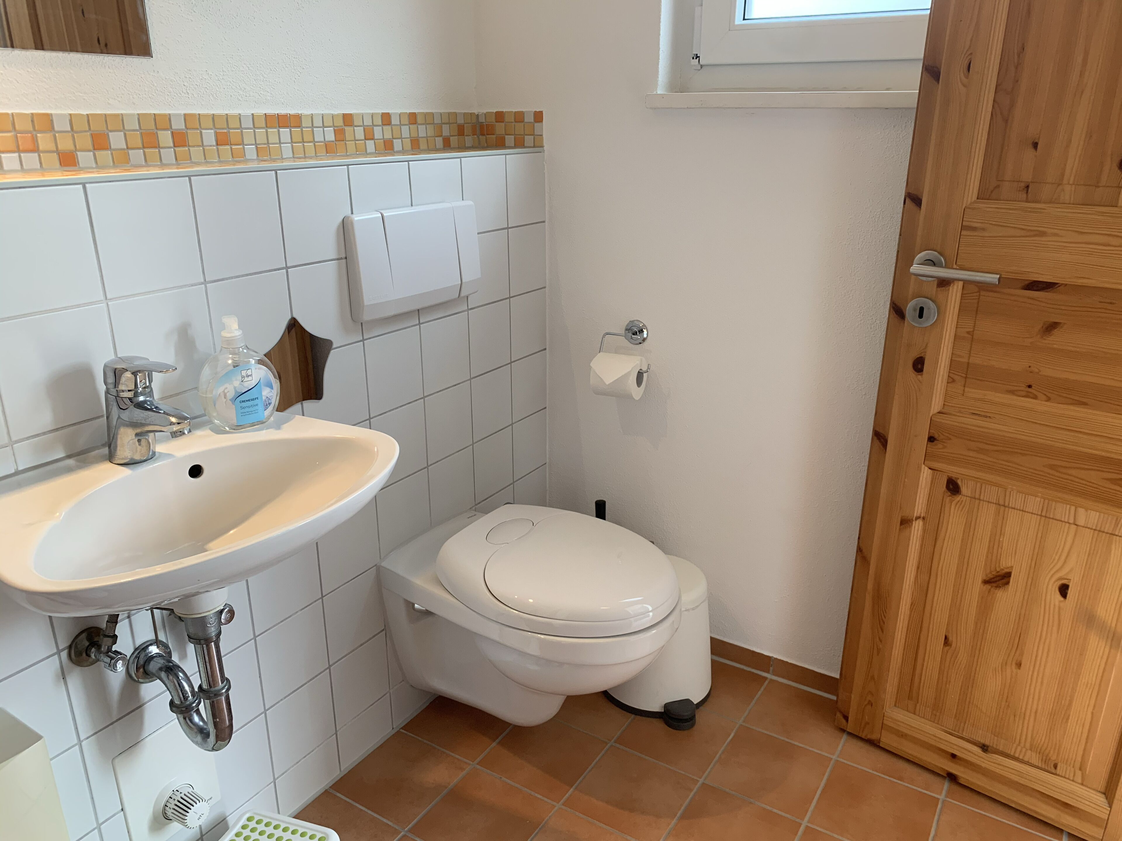 Une petite salle de bain avec un lavabo blanc, des toilettes et une porte en bois.