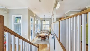 Un pasillo espacioso con una escalera de madera, un comedor con una mesa redonda y sillas, y un sofá verde.
