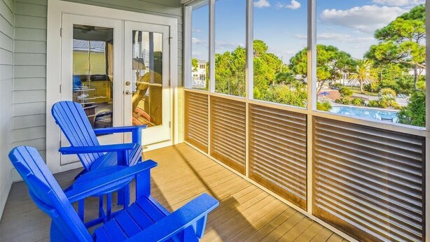 Un porche cubierto con sillas Adirondack azules, una puerta corrediza de vidrio y vistas a una piscina y árboles.