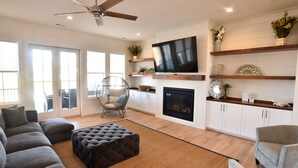 A modern living room with a sectional sofa, ottoman, and a fireplace. - New 5 bedroom house in Bayside Village by the beach! (Cape Charles)