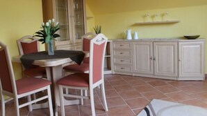 A dining area with a table and chairs, a cabinet, and a shelf with items. - Cozy apartment with a view of the beautiful Spreewald. (Burg)