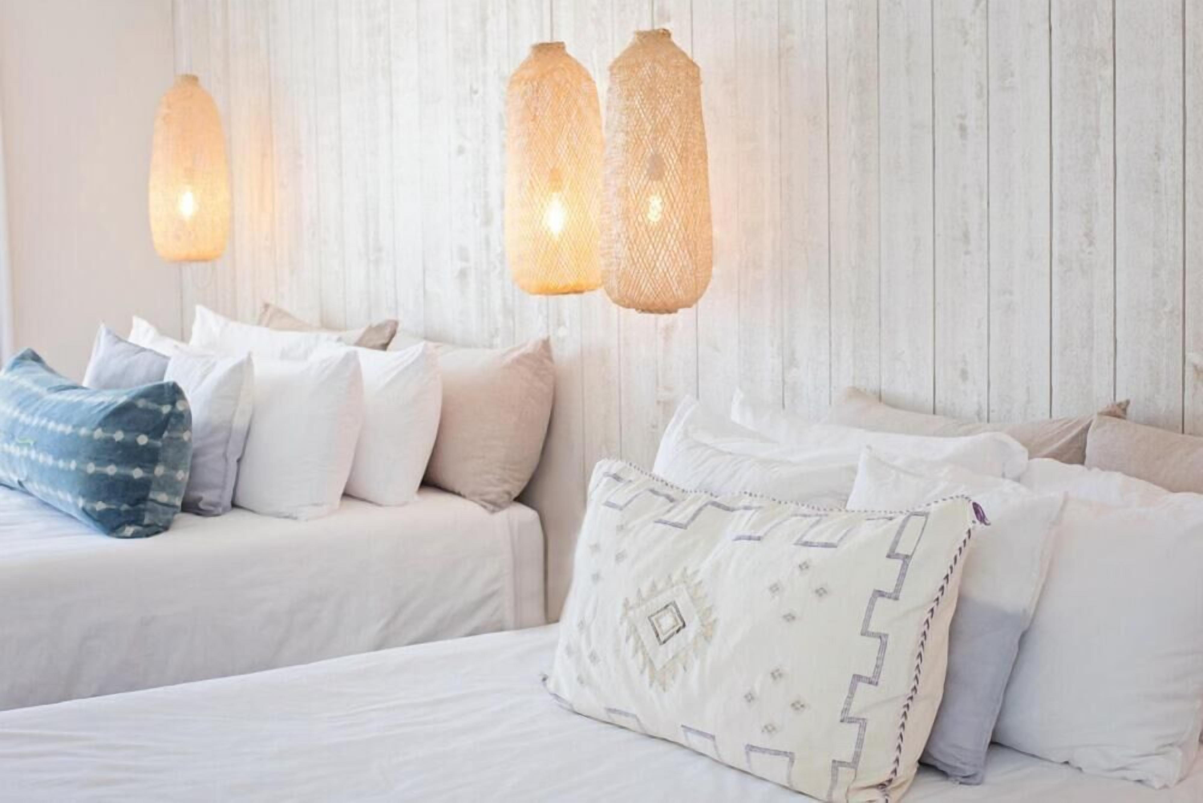 A bedroom with two beds, white bedding, and patterned pillows.