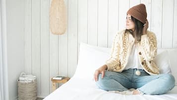 Una persona sentada en una cama en una habitación con paredes blancas y suelo de madera.