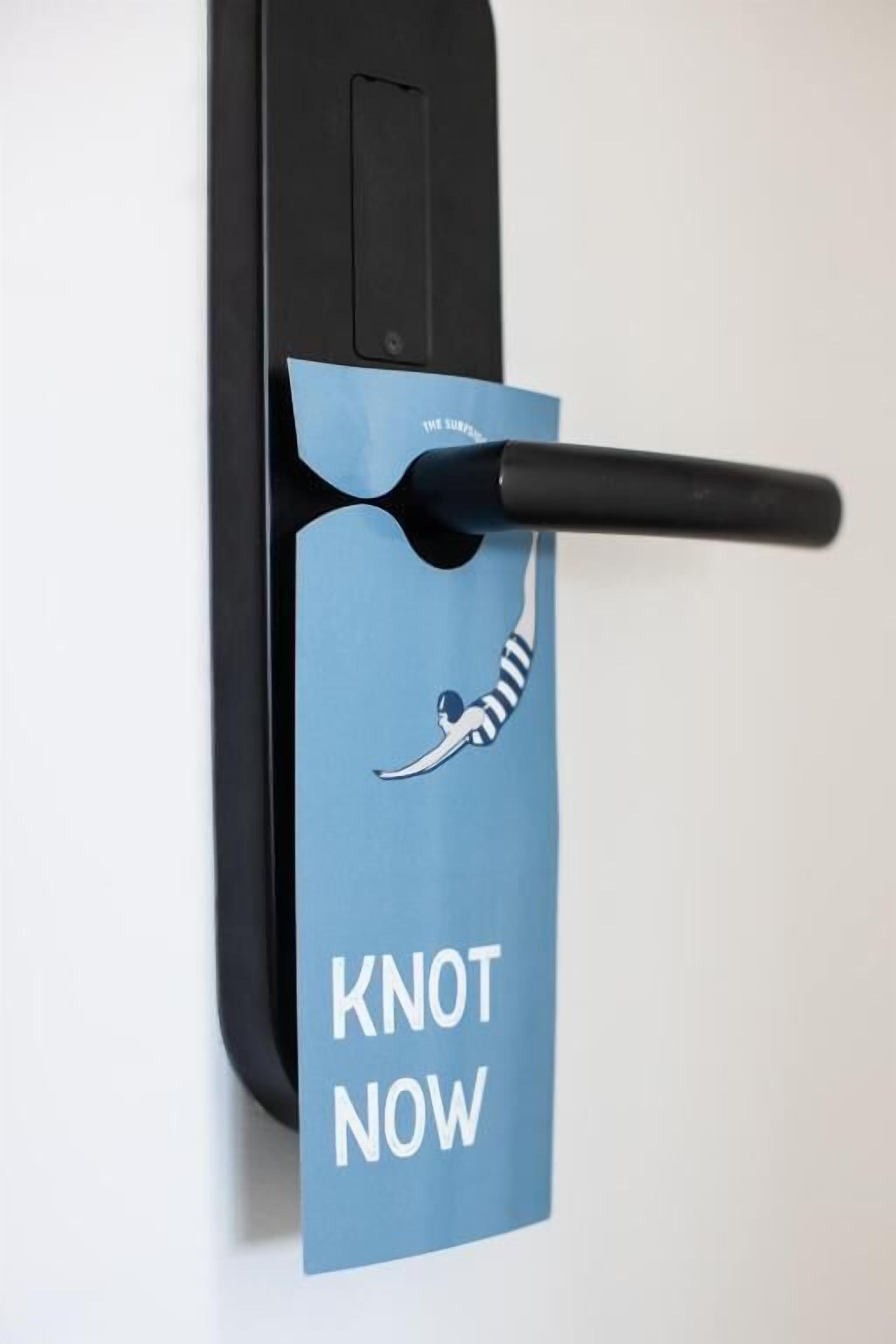A door handle with a blue card that reads "KNOT NOW" and a graphic of a person tied with a rope.