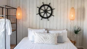Un dormitorio con pared de madera, una cama con ropa de cama blanca, un adorno con timón de barco y dos lámparas colgantes.