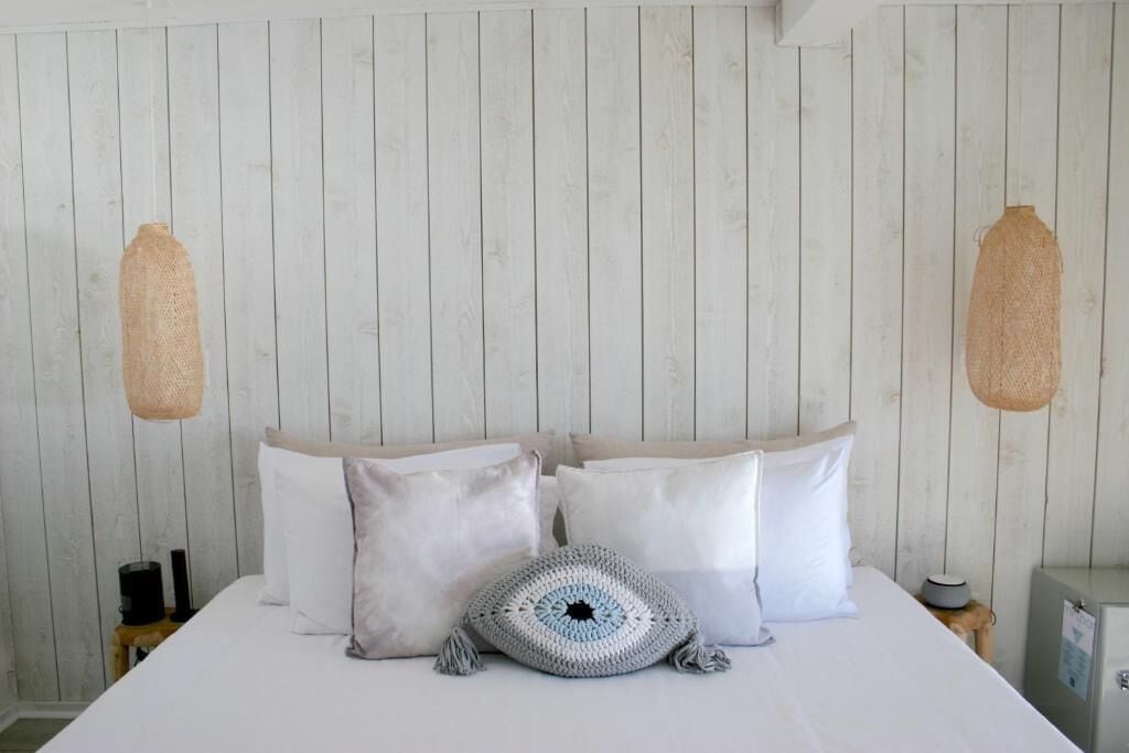 A bedroom with a bed, white pillows, a crocheted throw, and a wooden wall.