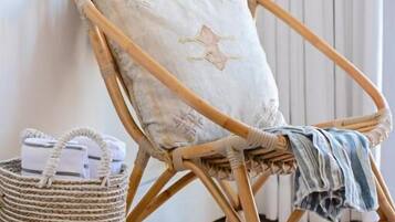 Una silla de mimbre con un cojín apoyada contra una pared, una cesta tejida con objetos, y una manta a rayas sobre el suelo.