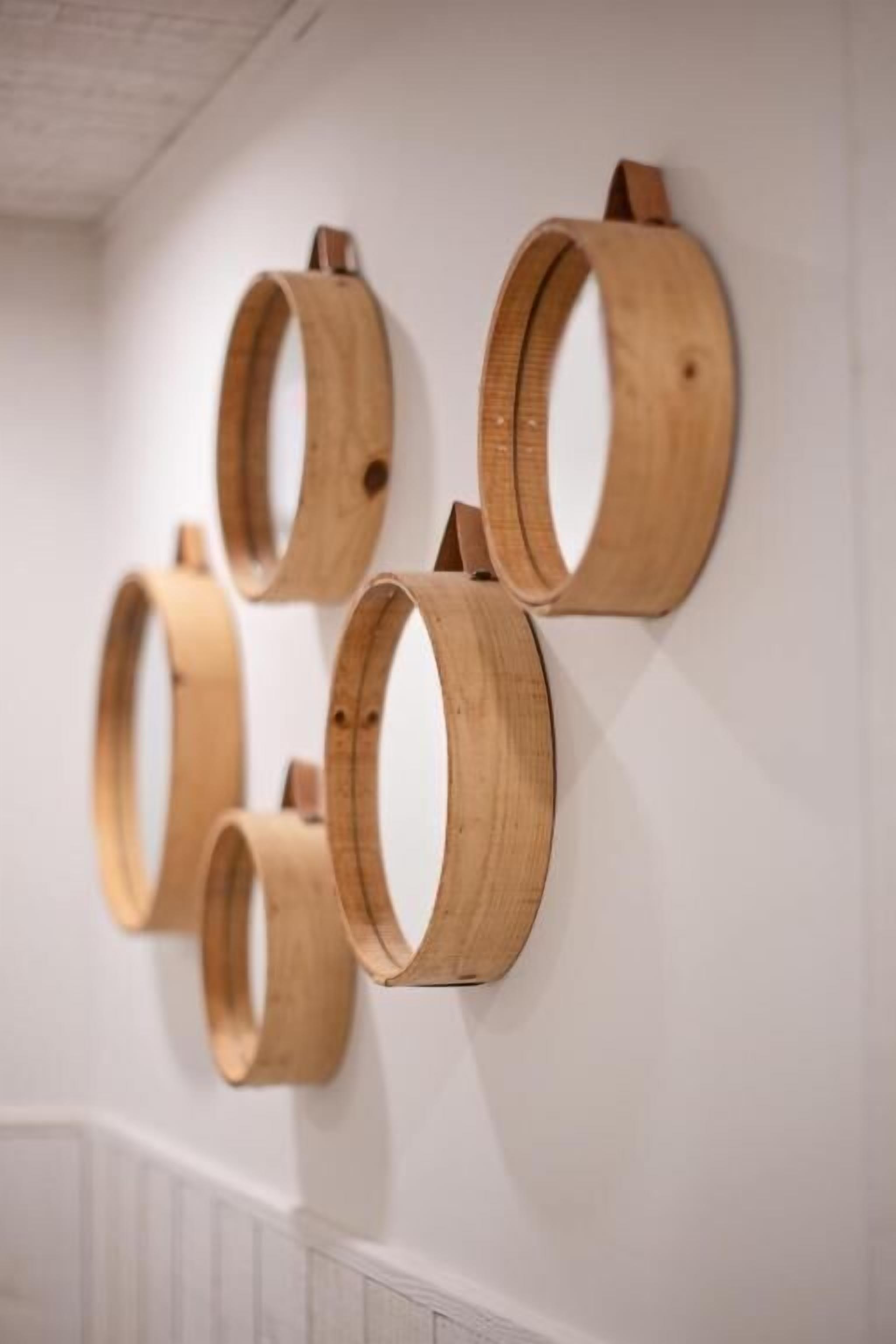 Un mur orné de cinq miroirs en forme de tonneau, tous en bois et de tailles différentes.