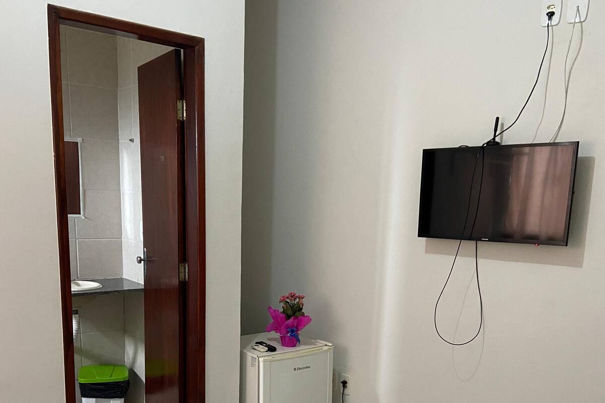 Ett hotellrum med en säng, en tv som är monterad på väggen, ett litet kylskåp och ett badrum som syns genom en öppen dörr.