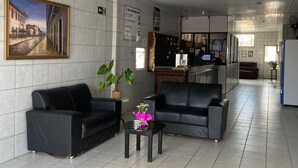 Een hotel lobby met zwarte leren banken, een betegelde vloer, een schilderij van een straatbeeld en een receptiebalie.