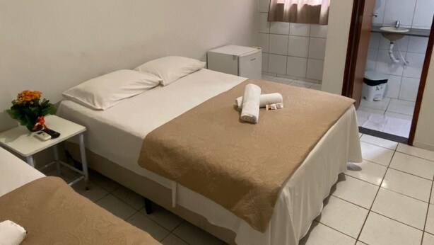 Hotelkamer met twee bedden, een klein nachtkastje met een bloevas, een airconditioner, een raam met gordijnen en een badkamer die door een geopende deur zichtbaar is.