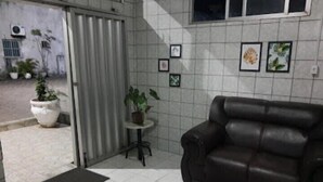 Een kamer met een donkerbruine leren bank, een klein rond tafeltje met een bloempot en een betegelde vloer.