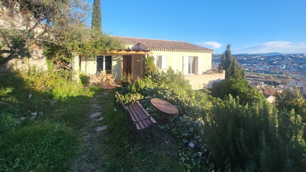 A house with a tiled roof, a garden with a bench, and a view of a cityscape. - Villa 90 m² panoramic view Nice, sea and mountains (Saint-Laurent-du-Var)