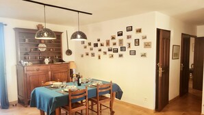 A dining area with a table set for four, a wooden cabinet with dishes, and a wall adorned with framed pictures. - Villa 90 m² panoramic view Nice, sea and mountains (Saint-Laurent-du-Var)