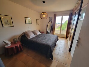 A bedroom with a bed, a bedside table, a lamp, a mirror, and a sliding glass door leading to a balcony.