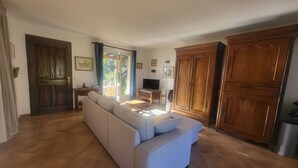A living room with a sofa, a television, a wooden cabinet, and a sliding glass door leading to an outdoor area. - Villa 90 m² panoramic view Nice, sea and mountains (Saint-Laurent-du-Var)