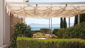 A covered outdoor area with a view of the sea, potted plants, and neatly trimmed hedges. - 2: GROUND FLOOR- APARTMENT ON THE SEA (Alcúdia)