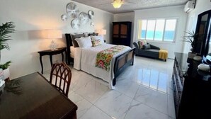 A spacious bedroom with a bed, a desk, and a chair. There is a window with a view of the ocean. - The View ll! (Christiansted)