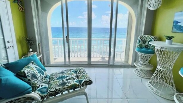 A balcony with a view of the ocean, a white chair, a patterned sofa, and a small table. - The View ll! (Christiansted)
