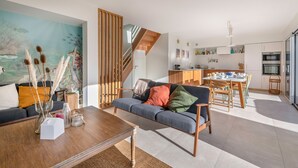 Una sala moderna con sofá, mesa de centro y un cuadro en la pared. Una escalera conduce a un nivel superior.