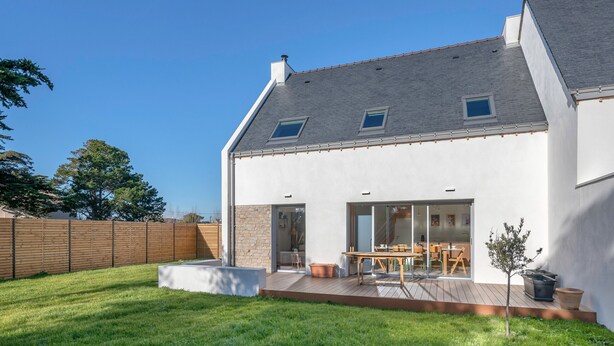 Una casa moderna con una terraza amplia, un patio trasero cercado y un cielo despejado.