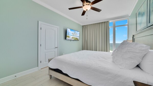 A bedroom with a bed, a ceiling fan, a door, a window with curtains, and a painting on the wall. - New Complex!! New to the Rentals Market. Beachfront, Lazy River and Slide! (Orange Beach)