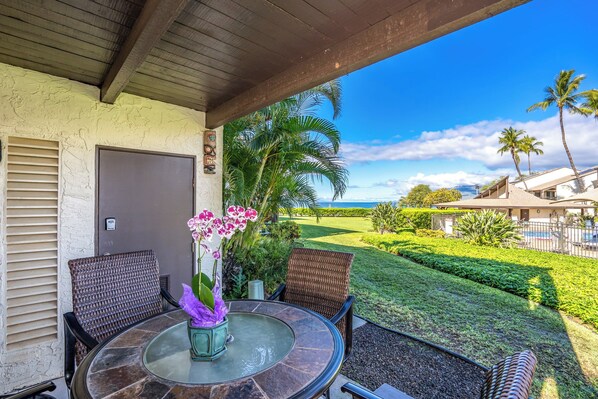 An outdoor patio with a round table, wicker chairs, and a view of a golf course and ocean.