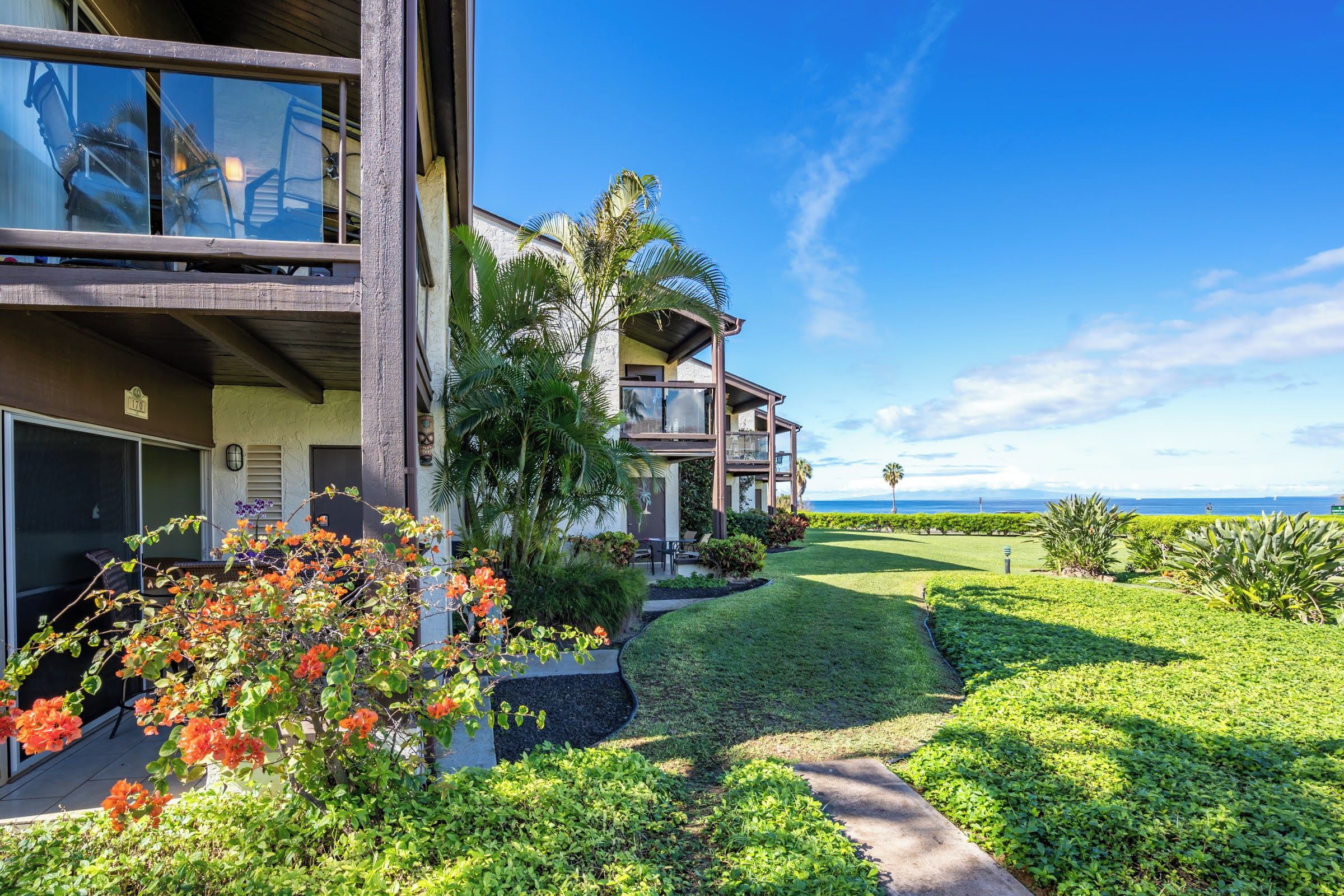 A modern multi-story building with a well-maintained lawn and tropical plants.