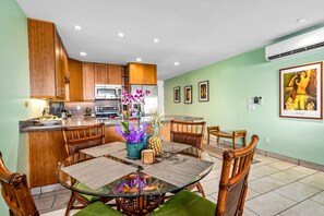 A modern kitchen with wooden cabinets, a central island, and a dining area with a glass table and wicker chairs.