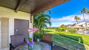 An outdoor patio with a round table, wicker chairs, and a view of a golf course and ocean. - Hale Kamaole #170, Fully Renovated, Ground Floor, Full A/C, Near Kamaole III (Kihei)