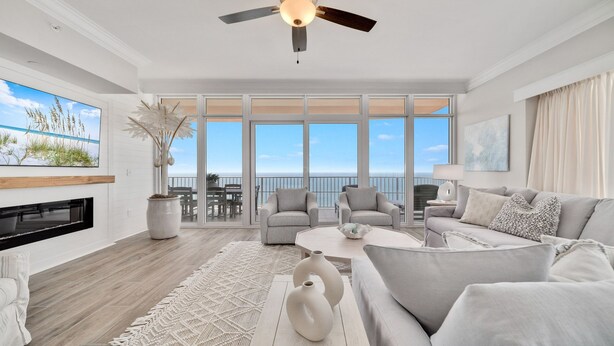 A spacious living room with a large window overlooking the ocean, a ceiling fan, and a fireplace. - New Complex!! New to the Rentals Market.  Beachfront, Lazy River and Slide! (Orange Beach)