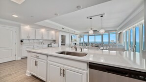 A spacious kitchen with white cabinetry, a large island with a sink, and a view of the ocean through large windows. - New Complex!! New to the Rentals Market.  Beachfront, Lazy River and Slide! (Orange Beach)