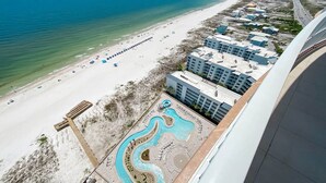 An aerial view of a beach resort with a swimming pool, beach umbrellas, and a hotel with multiple buildings. - New Complex!! Beachfront, Lazy River and Slide! Unmatched Views!! (Orange Beach)