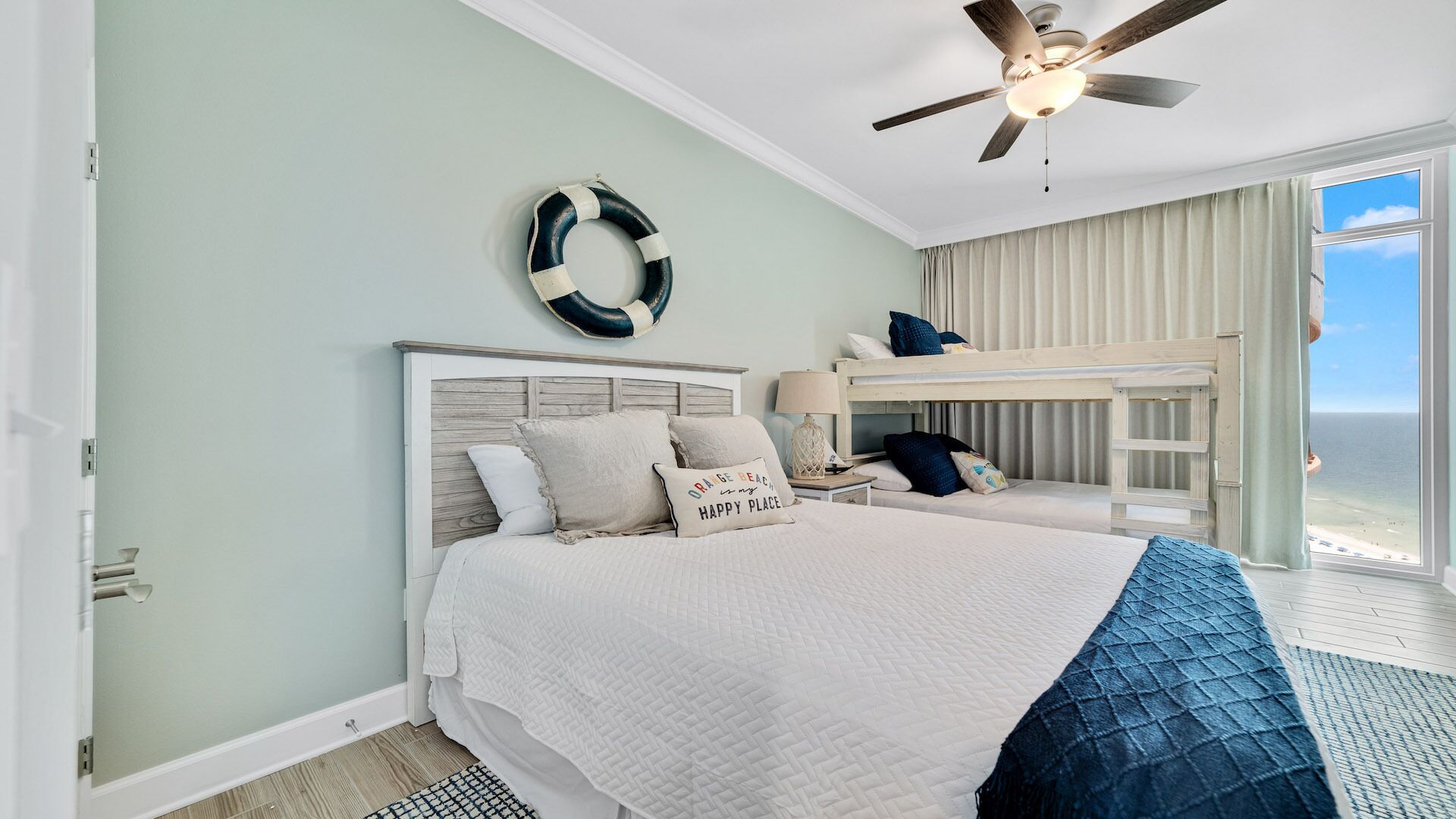 A bedroom with a bed, a ceiling fan, a view of the ocean, and a bunk bed.
