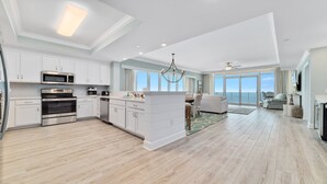 A modern kitchen with built-in appliances, a dining area with a view, and a spacious living room with a balcony. - New Complex!! Beachfront, Lazy River and Slide! Unmatched Views!! (Orange Beach)