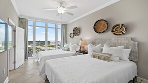 Une chambre d’hôtel avec deux lits, un ventilateur de plafond, de grandes fenêtres et une vue sur la ville.